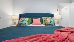 Un dormitorio con un cabecero capitonado, una cama con colcha azul y almohadas florales de colores.