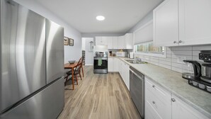 A modern kitchen with stainless steel appliances, white cabinets, and a wooden dining table.