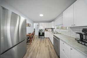 A modern kitchen with stainless steel appliances, white cabinets, and a wooden dining table.