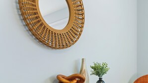 A black dresser with three drawers, a woven mirror above it, and a small potted plant on top.