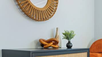 Une commode noire à trois tiroirs, un miroir à motifs tissés au-dessus, et une petite plante en pot posée sur le dessus.