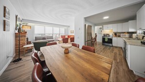 A modern kitchen with white cabinets, a wooden dining table, and a large window.