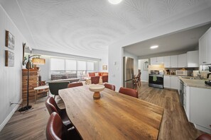 A modern kitchen with white cabinets, a wooden dining table, and a large window.
