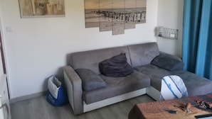 A living room with a grey sofa, a blue bag, and a wall-mounted shelf with a lamp. - T2 less than 50m from the beach in Beg Meil near Fouesnant (Fouesnant)