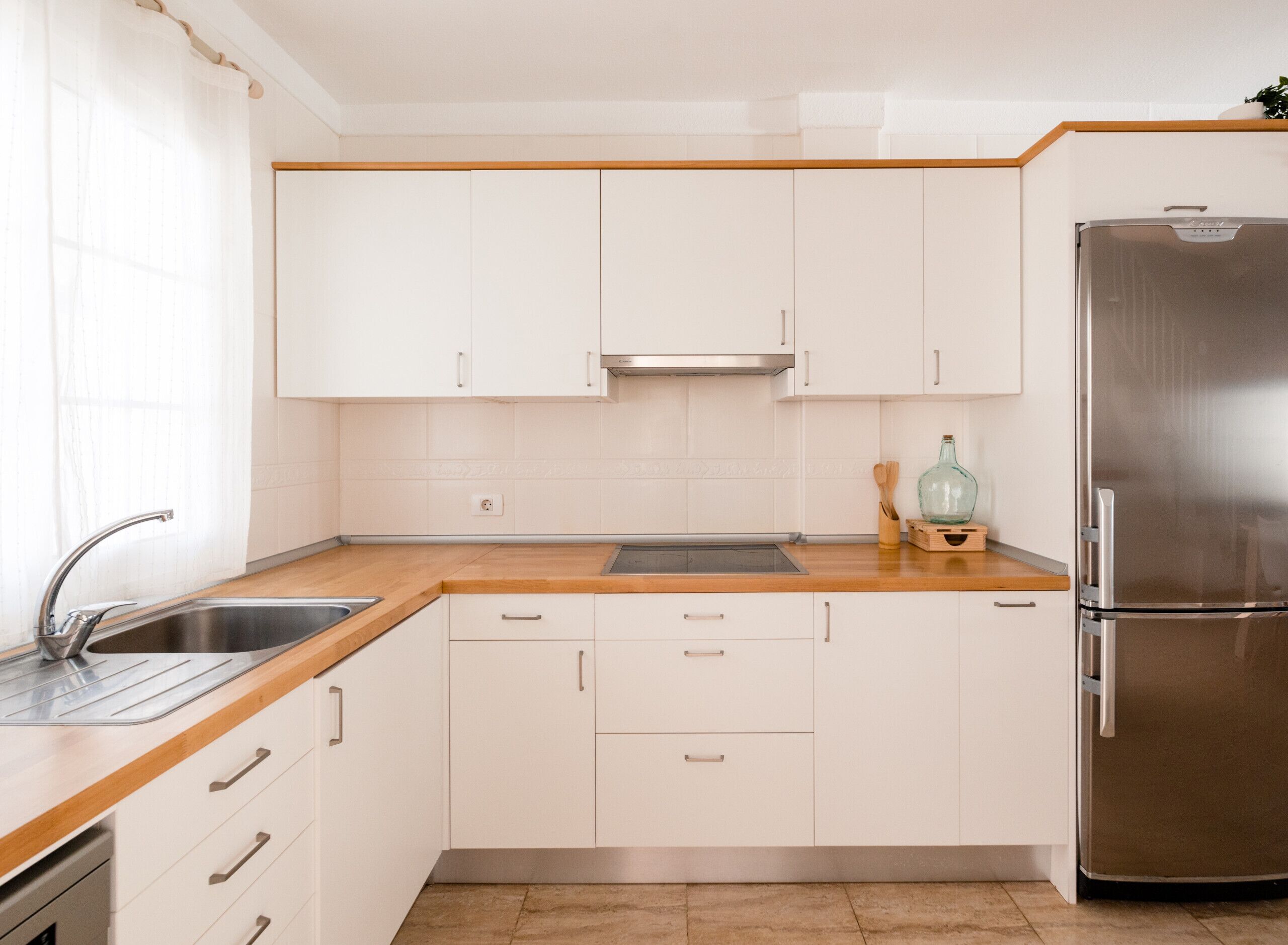 Eine moderne Küche mit weißen Schränken, einem Edelstahl-Kühlschrank, einer Holzarbeitsplatte und einem Spülbecken.