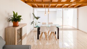 A modern dining area with a glass table and chairs, wooden ceiling beams, and potted plants. - Casa Da Roca Medano - Beach House & Terrace (Granadilla de Abona)