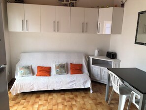 A room with a white sofa, orange pillows, a small table, and a white cabinet. - Pretty villa with swimming pool (Canet-en-Roussillon)