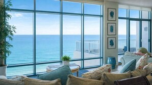Ein Zimmer mit großen Fenstern mit Meerblick, einer Couch, einem kleinen Tisch und einer Topfpflanze.