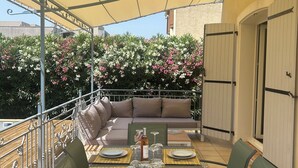 Eine Terrasse im Freien mit Esstisch, umgeben von grünen Stühlen und einer Couch mit Kissen.