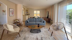 Ein Wohnzimmer mit einer Couch, zwei Sesseln, einem Couchtisch und einem Essbereich im Hintergrund.