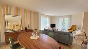 Ein modernes Wohnzimmer mit einem Holzesstisch, grünen und braunen Stühlen, einem grauen Sofa und einem großen Spiegel an der Wand.
