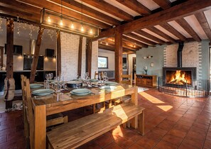Un comedor con una mesa de madera dispuesta para una comida, una chimenea y vigas de madera a la vista.