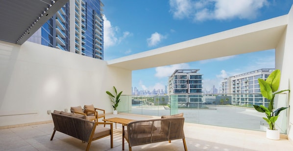 A modern balcony with a view of a city skyline, furnished with wicker chairs and a small table. - LUX District One Lagoon View Townhouse (Dubai)