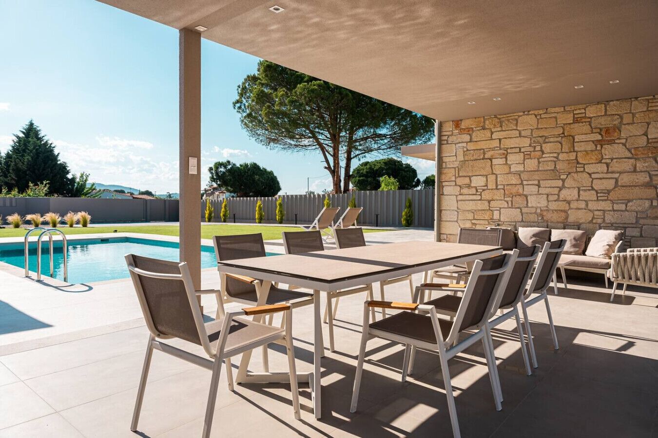 En udendørs terrasse med pool, et bord med stole og en stenvæg.