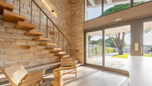 Un interior moderno con pared de piedra, escalera de madera y grandes puertas correderas de vidrio que dan a un espacio exterior.