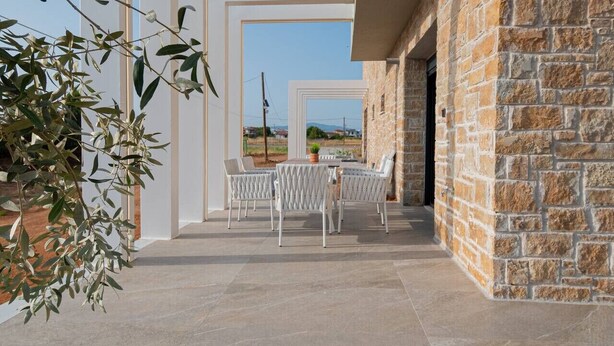 Un patio al aire libre con pared de piedra, sillas blancas y una mesa.