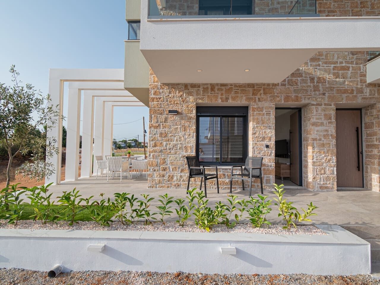 Un bâtiment moderne doté d’une façade en pierre, d’un espace extérieur couvert aménagé en coin salon et offrant une vue sur le paysage environnant.