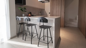 A modern kitchen with a central island, two bar stools, and a pendant light. - Theano Sea Suite 3 by Travel Pro Services (Portaria)