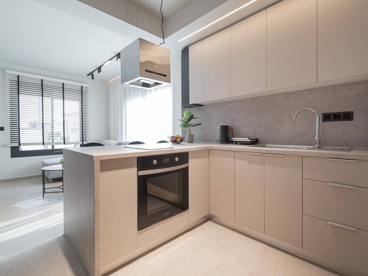 A modern kitchen with a built-in oven, a sink, and a window with blinds.