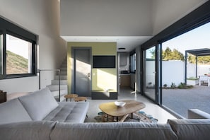 Uma sala de estar moderna com um sofá, mesa de centro e vista para o exterior por grandes janelas.