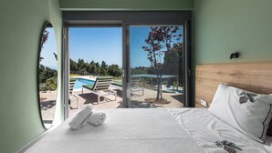 A bedroom with a large bed, a view of a pool and outdoor area through a sliding glass door.