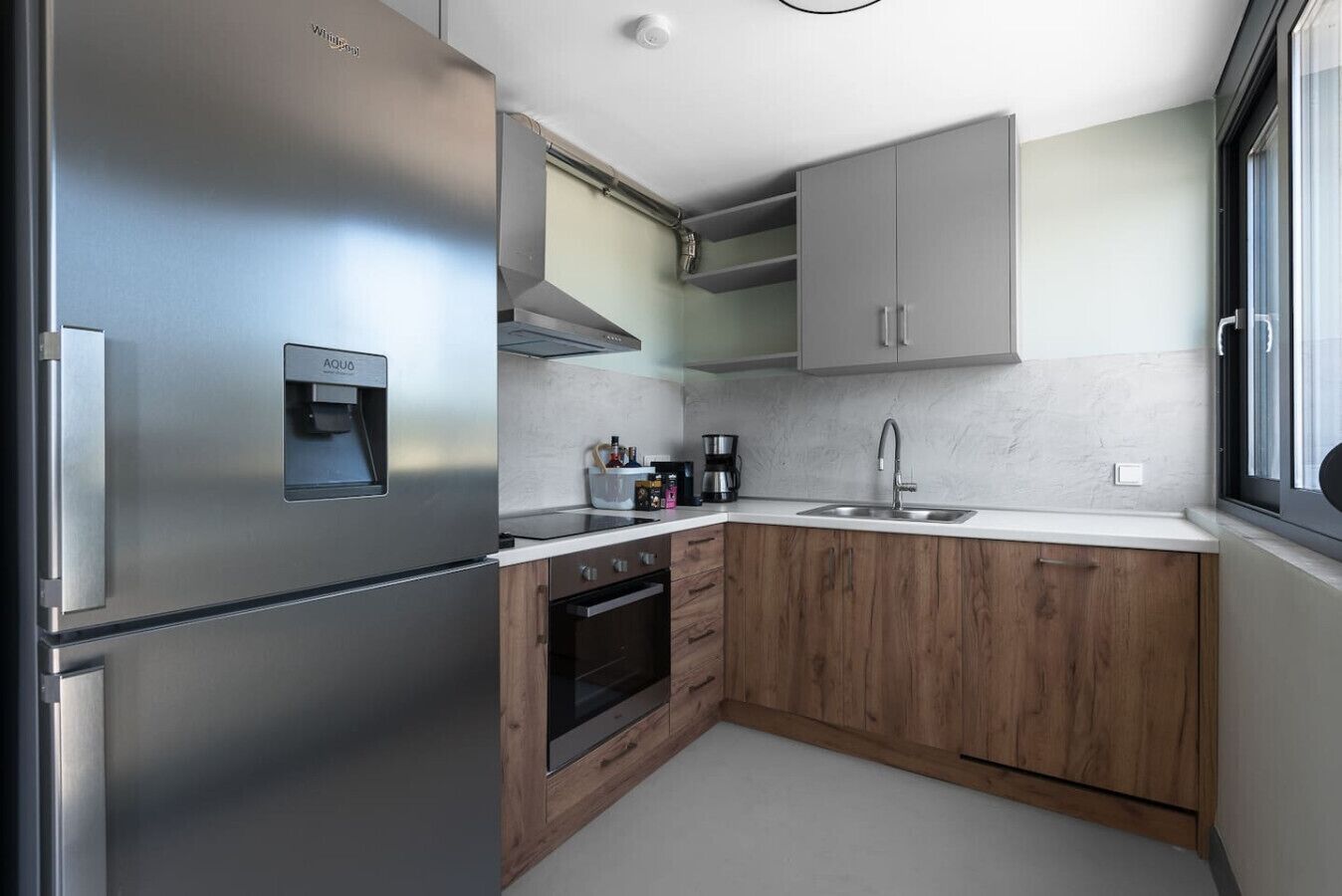 Eine kleine Küche mit einem Edelstahl-Kühlschrank, einem eingebauten Backofen, einem Spülbecken und Holzschränken.