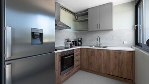 A compact kitchen with a stainless steel refrigerator, a built-in oven, a sink, and wooden cabinetry.