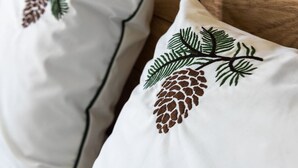 A pillow with a pine cone and fern embroidery.