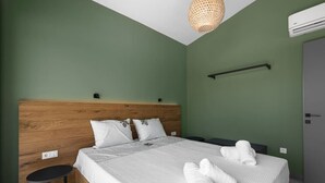 A neatly made bed with white linens and two rolled towels, a small round table, and a wooden headboard.
