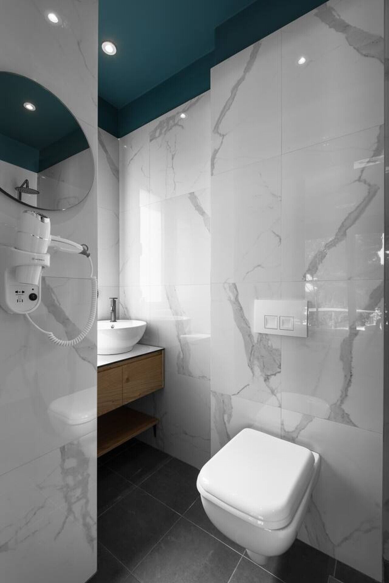 A modern bathroom with a marble wall, a white toilet, a wooden vanity, and a handheld showerhead.