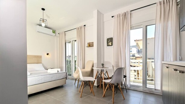 Ein modernes, helles Wohnzimmer mit einer Couch, einem Esstisch mit Stühlen und einem Balkon mit Vorhängen.