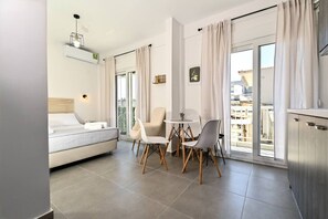 Een moderne, goed verlichte woonkamer met een bank, een eettafel met stoelen en een balkon met gordijnen.