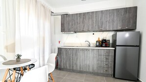 Eine moderne Küche mit grauen Schränken, einem Edelstahlkühlschrank und einer kleinen Essecke mit einem weißen Tisch und Stühlen.