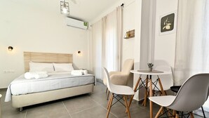 Ein modernes Hotelzimmer mit einem Bett, einem kleinen runden Tisch, zwei Stühlen und einer wandmontierten Klimaanlage.