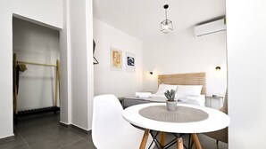 Ein modernes Hotelzimmer mit einem Bett, Nachttisch und einem runden Tisch mit Stühlen. Auf dem Tisch steht eine kleine Pflanze, eine Wandklimaanlage und eine Deckenleuchte.