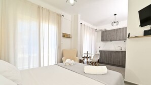 Ein Hotelzimmer mit Bett, Sessel, kleinem Tisch, Fernseher und Küchenzeile.