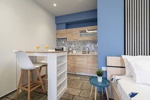 A compact room with a bed, a small table with two chairs, a kitchenette, and a small round table with a plant. - Kallinest Studio by RentalsPro - Kallithea (Kallithea)