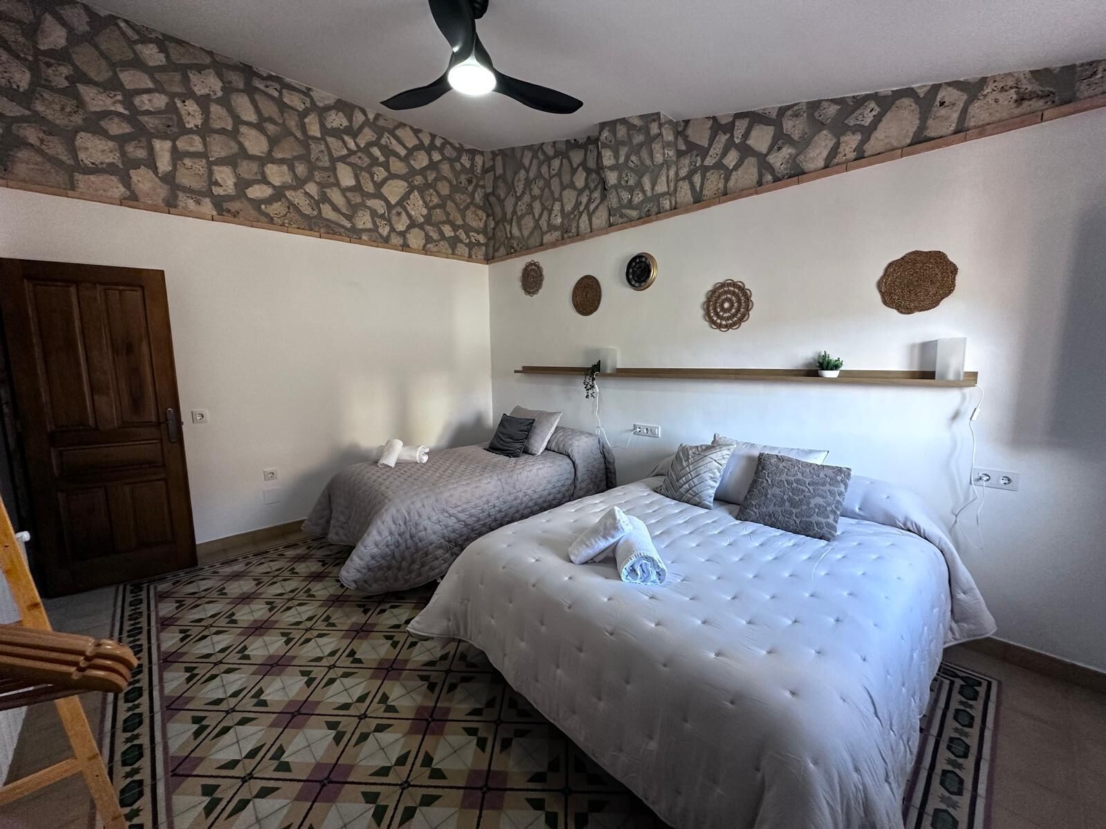 Un dormitorio con dos camas, una pared de piedra, un ventilador de techo y un suelo estampado.