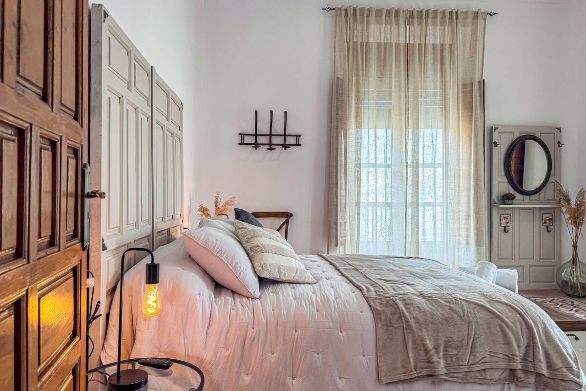 Une chambre à coucher comprenant un lit, une lampe de chevet, une armoire en bois et un miroir.