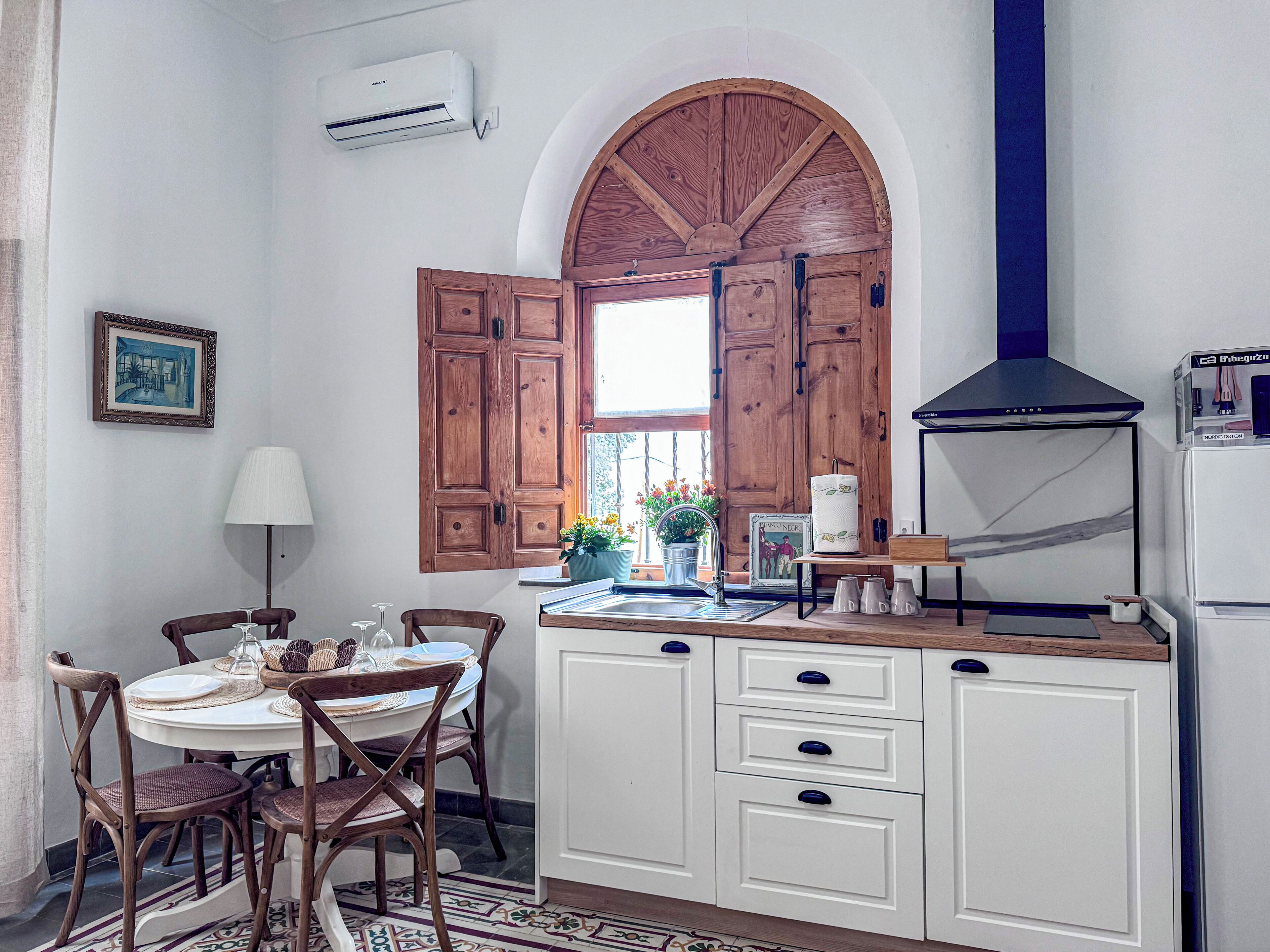 Una cocina con armarios de madera, horno empotrado, ventana con contraventanas de madera y una planta en maceta en el alféizar.