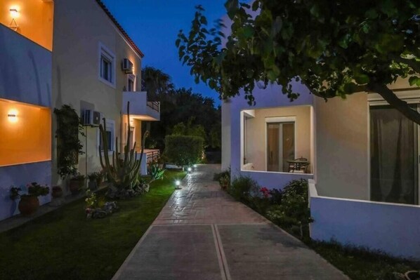 A pathway leading to a modern building with outdoor seating and a well-lit entrance.