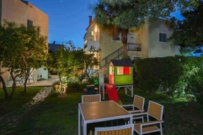 En terrasse med et bord og stole, et lille legehus og en trappe op til en etage.