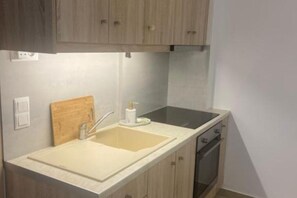 A kitchen with a sink, wooden cabinets, a countertop, a stove, and a wooden cutting board.