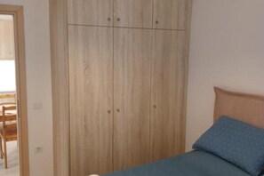 A bedroom with a bed, a wooden wardrobe, and a chair in the background.