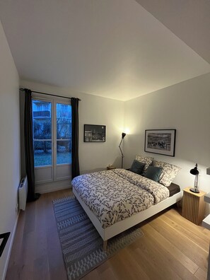 Ein Schlafzimmer mit einem Bett, einem Nachttisch, einer Stehlampe und einem Fenster mit Vorhängen.