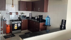 A kitchen with dark wooden cabinets, a gas stove, a microwave, and a water dispenser. - Paradise Villa just outside Paradise/Karura forest for Nature visit,walks & more (Kiambu)