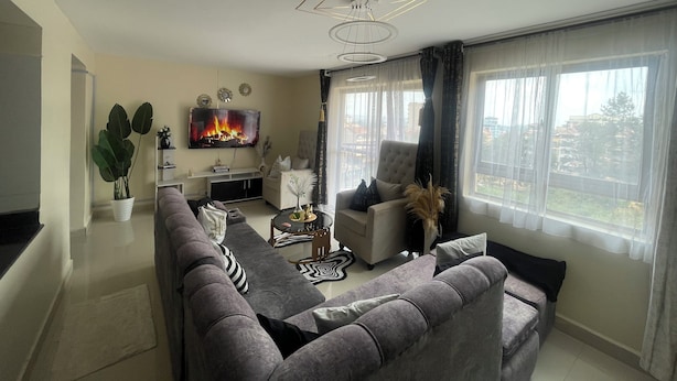 A modern living room with a grey sofa, a flat-screen TV, and a fireplace. - Paradise Villa just outside Paradise/Karura forest for Nature visit,walks & more (Kiambu)