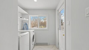 Une buanderie équipée d’un lave-linge, d’un sèche-linge et d’une fenêtre donnant sur les arbres.