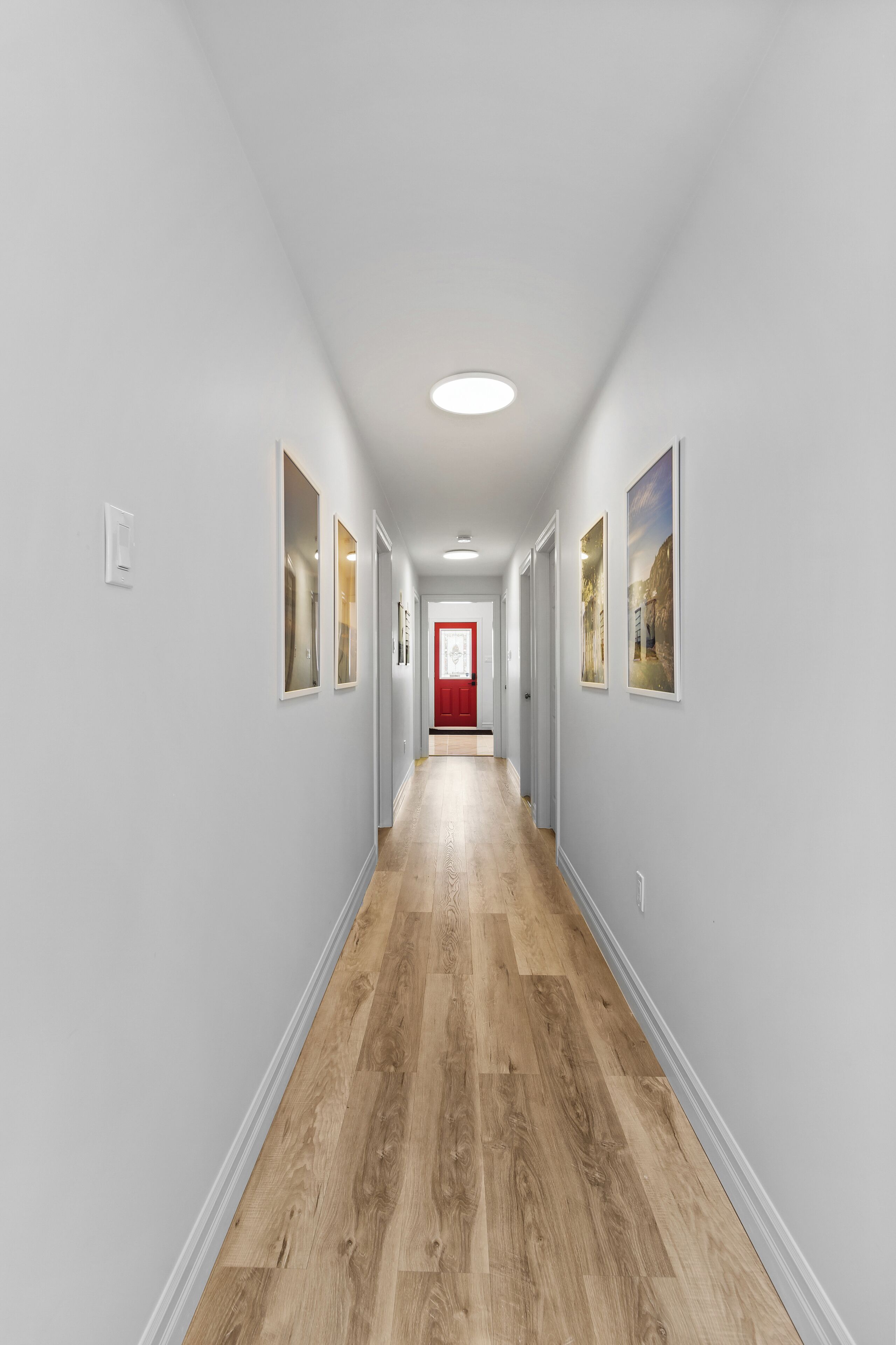 A hallway with light gray walls, wooden flooring, and framed pictures on the walls.