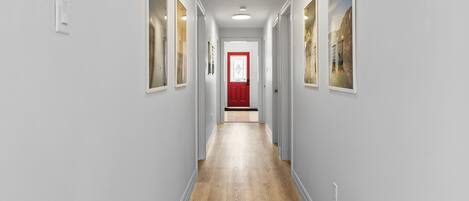 A hallway with light gray walls, wooden flooring, and framed pictures on the walls.